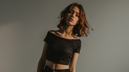 Fototapeta premium Female top model wearing casual cropped top and trousers in front of gray background