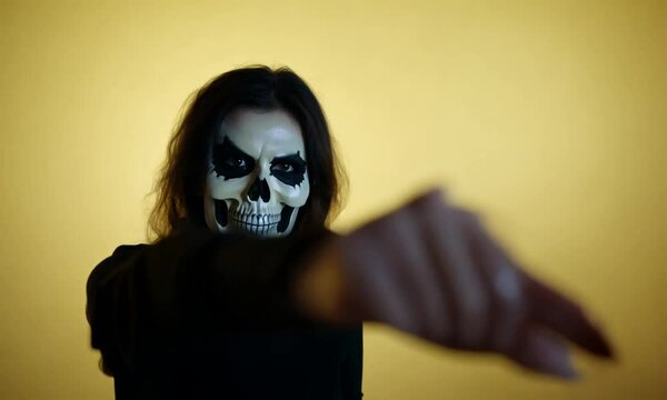 Happy Halloween concept. Scared horrible female in special outfit, wears white clay skull, professional makeup to look spooky, wears black clothes points away. hyper-realistic 4K video