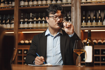 Professional Looking Sommelier Drinking Red Wine in Glass During Tasting Session, Sitting at Table Being in Cellar