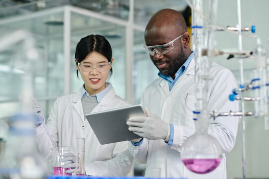 Two young intercultural chemists looking at screen of tablet held by African American male scientist while carrying out new trial