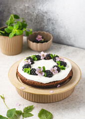 Delicious homemade dark chocolate cake with vanilla cream decorated with blackberries, blossoms and lemon balm leaves. Sweet food concept.