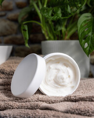  Opened cream jar with blank lid on brown bath towel, near plant, cosmetic mockup
