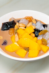 angle view bowl of milktea flavor syrup mixed with grass jelly and mangoes and peach gum and tapiocas and red beans and guiling jelly etc. at vertical composition