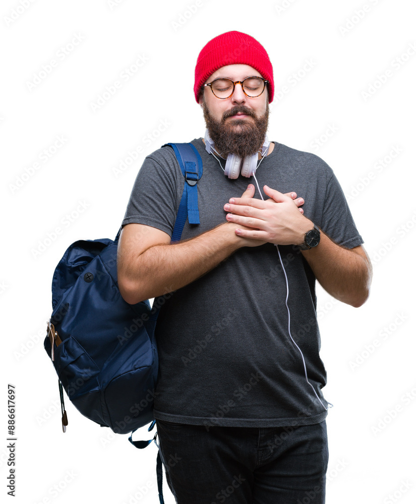 Sticker Young hipster man wearing red wool cap and backpack over isolated background smiling with hands on chest with closed eyes and grateful gesture on face. Health concept.