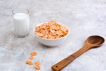bowl of corn granola with milk, fresh raspberries, blueberries . milk in a jug and a glass  on white wooden board for healthy breakfast