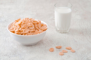 bowl of corn granola with milk, fresh raspberries, blueberries . milk in a jug and a glass  on white wooden board for healthy breakfast