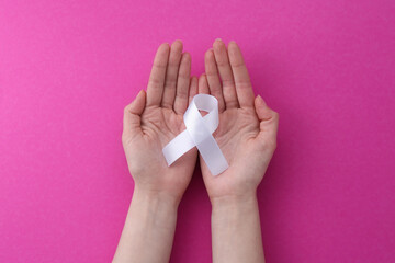 Woman with white awareness ribbon on pink background, top view