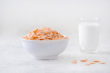 bowl of corn granola with milk, fresh raspberries, blueberries . milk in a jug and a glass  on white wooden board for healthy breakfast