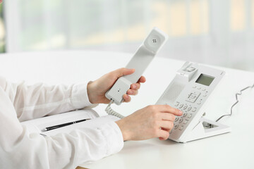 Fototapeta premium Assistant dialing number on telephone against blurred background, closeup