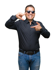 Fototapeta premium Middle age arab man wearing sunglasses over isolated background smiling making frame with hands and fingers with happy face. Creativity and photography concept.