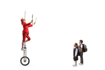 Girl and boy watching an acrobat riding a giraffe unicycle and juggling