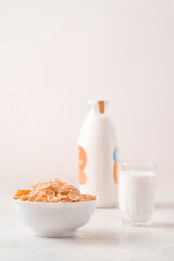bowl of corn granola with milk, fresh raspberries, blueberries . milk in a jug and a glass  on white wooden board for healthy breakfast