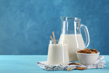 Glass of almond milk, jug and almonds on light blue wooden table, space for text