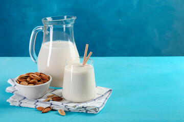 Glass of almond milk, jug and almonds on light blue wooden table, space for text