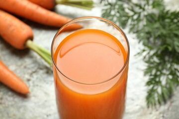 Fresh carrot juice in glass and vegetables on grey table, closeup