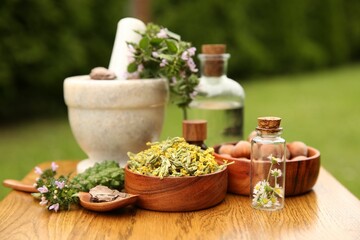 Different ingredients for tincture, bottles, mortar and pestle on wooden table outdoors