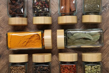 Different spices in glass jars on wooden table, flat lay