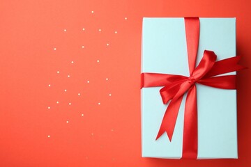 Gift box with red bow and confetti on coral background, top view. Space for text
