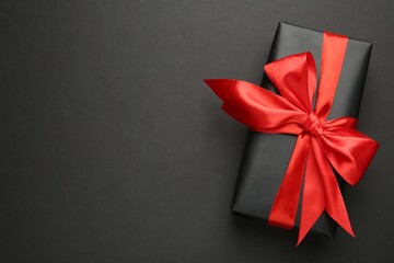 Gift box with red bow on black background, top view. Space for text