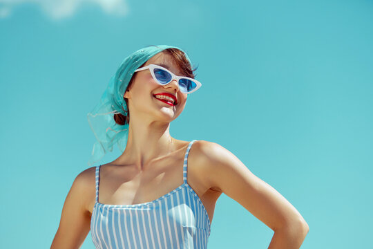 Woman in blue and white striped swimsuit, smiling broadly, under bright blue sky, embodying retro summer joy. Concept of hot summer holiday, weekends, vacation, relaxation.