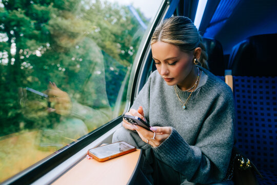 Attractive caucasian woman using a smartphone in regional train. Young beautiful woman using public transportation.