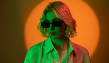 Stylish woman in sunglasses exudes chic attitude under colorful lighting in a vibrant setting