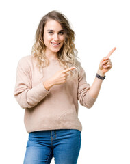 Beautiful young blonde woman wearing sweatershirt over isolated background smiling and looking at the camera pointing with two hands and fingers to the side.