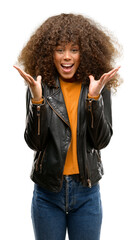 African american woman wearing a leather jacket very happy and excited, winner expression celebrating victory screaming with big smile and raised hands