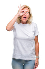 Fototapeta premium Middle age blonde woman over isolated background doing ok gesture shocked with surprised face, eye looking through fingers. Unbelieving expression.