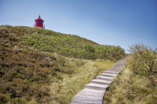 Wooden boardwalk through the sand dunes leading towards a lighthouse, Amrum, North Frisia, North Frisian Islands, Nordfriesland, Schleswig-Holstein, Germany