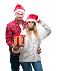 Young couple in love wearing christmas hat and holding present over isolated background with angry face, negative sign showing dislike with thumbs down, rejection concept