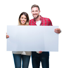 Young couple together holding blank banner over isolated background with a happy face standing and...