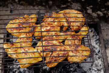 Juicy, seasoned chicken pieces are grilled to perfection on a metal grill over hot coals, capturing the essence of a rustic outdoor barbecue experience.