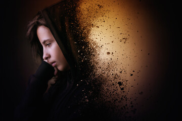 Conceptual portrait of a sad teenage girl wearing a hoodie disintegrating