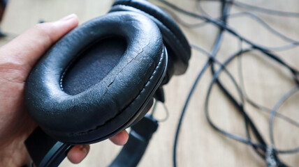 A person holding a black headphone, with a close up detail of the broken ear cup headphones cushion...