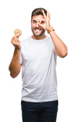 Young handsome man eating chocolate chips cookie over isolated background with happy face smiling doing ok sign with hand on eye looking through fingers