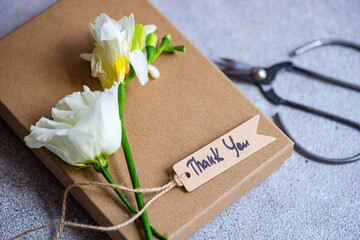 White freesia and Godetia flowers on top of a gift box with a thank you gift tag and scissors