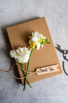 White freesia and Godetia flowers on top of a gift box with a thank you gift tab and scissors