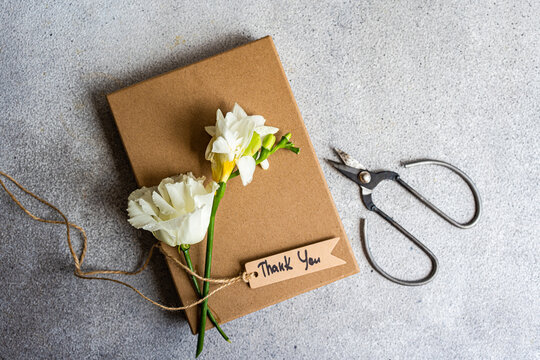 White freesia and Godetia flowers on top of a gift box with a thank you gift tag and scissors