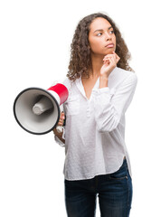 Young hispanic woman holding megaphone serious face thinking about question, very confused idea