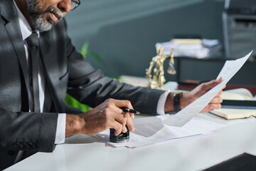 Cropped shot of mature male adviser or director of company putting stamp on documents while sitting...