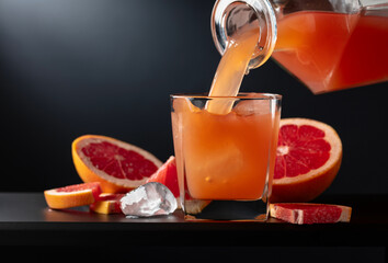 Glass of grapefruit juice with ice on a black background.