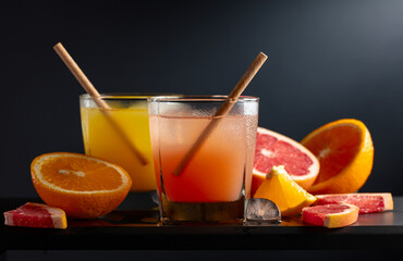 Glasses of grapefruit and orange juice with ice on a black background.