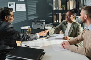 Happy young African American female specialist shaking hand of mature male director of business...