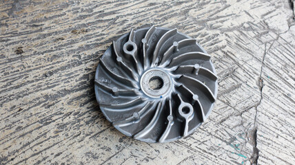 Obraz premium A close-up image of a silver motorcycle part on a textured surface. A close up of a silver Continuously Variable Transmission roller plate on a concrete surface background