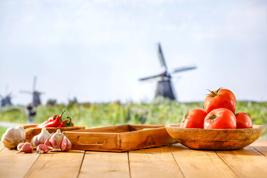 Wooden table with red tomatoes  and garlic with green fiels in countryside background. Copy space for products. Vegetables concept in autumn garden.