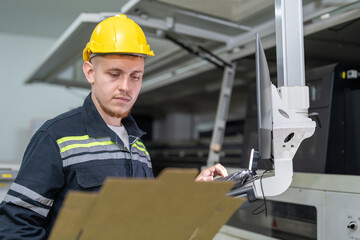 Male engineer checking quality cardboard box parts cutting from laser CNC machine in paper factory. Man technical in uniform wearing helmet safety operate and maintenance machine