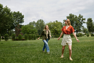 A young couple laughs and walks through a green park on a sunny day.