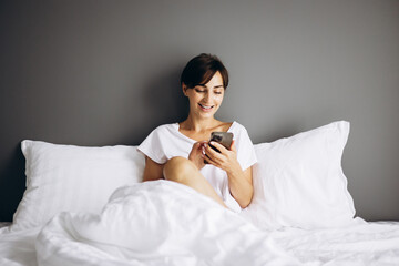 Young woman lying in her bed at home and using mobile phone