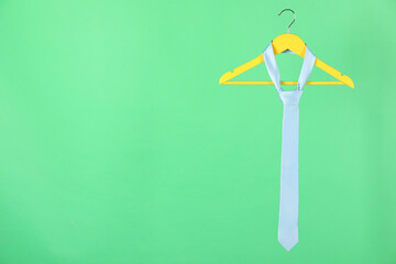 Hanger with light blue tie on green background. Space for text